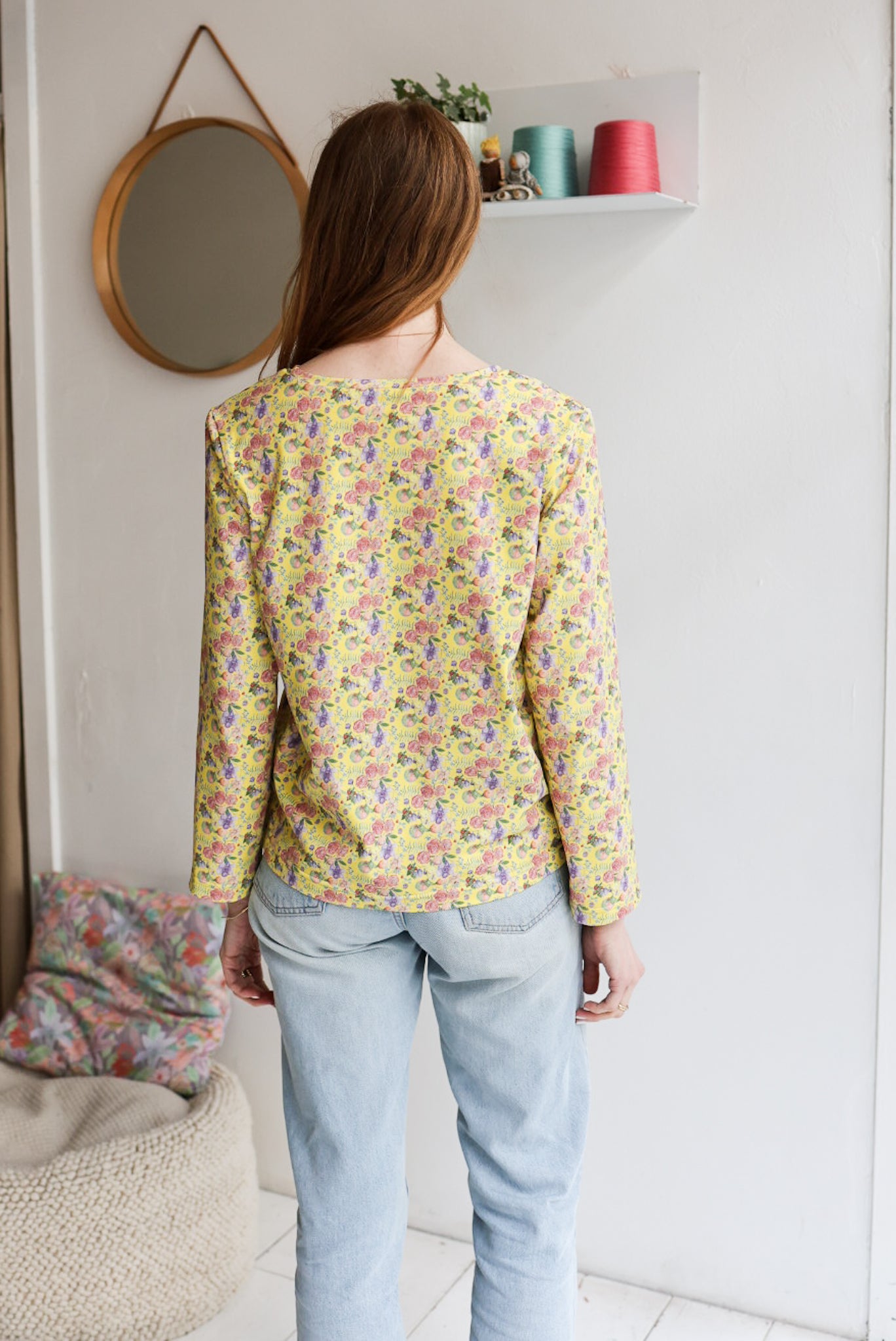 Woman wearing a floral patterned loose long sleeve t-shirt and jeans indoors.