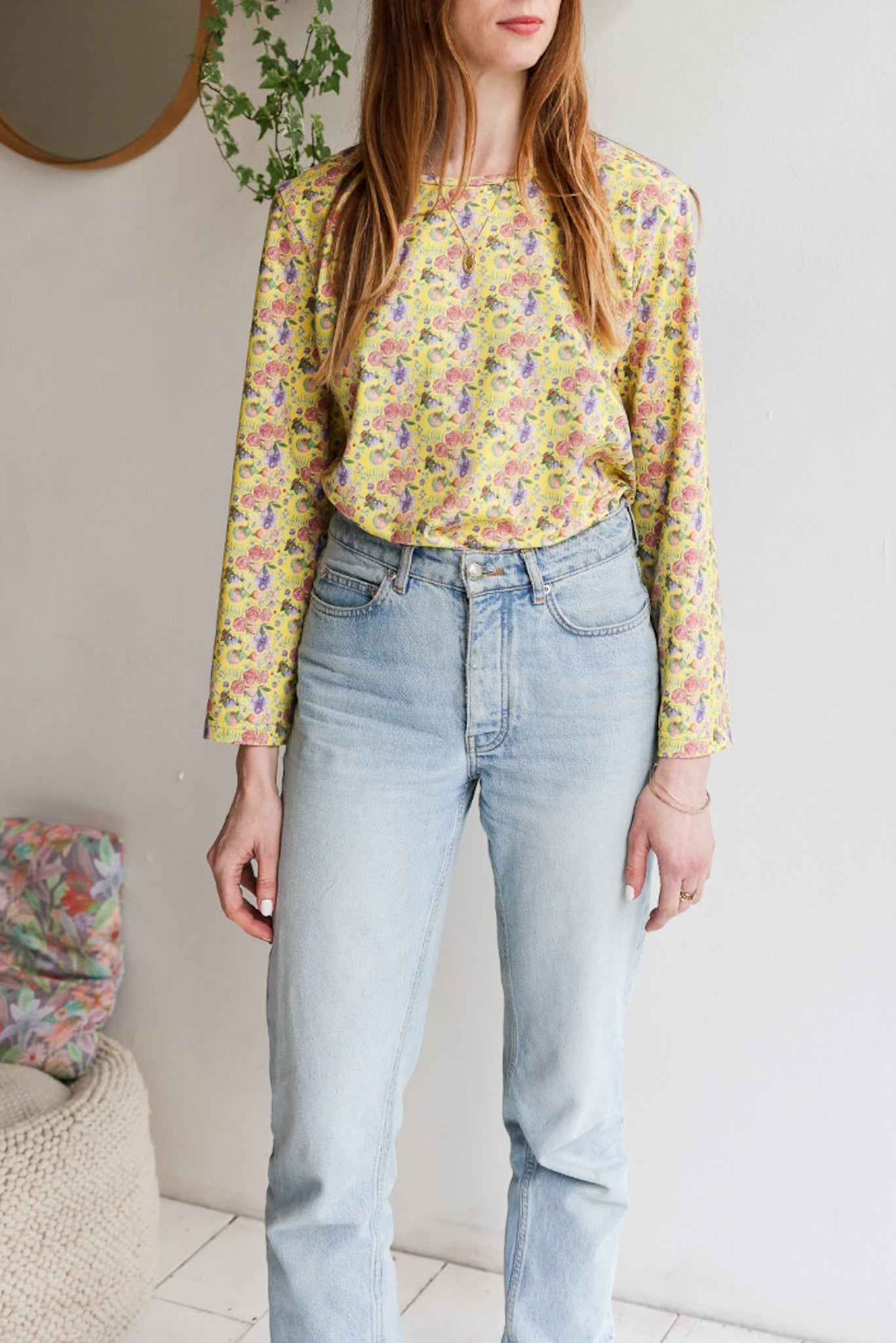 Woman wearing a floral patterned loose long sleeve t-shirt and jeans indoors.