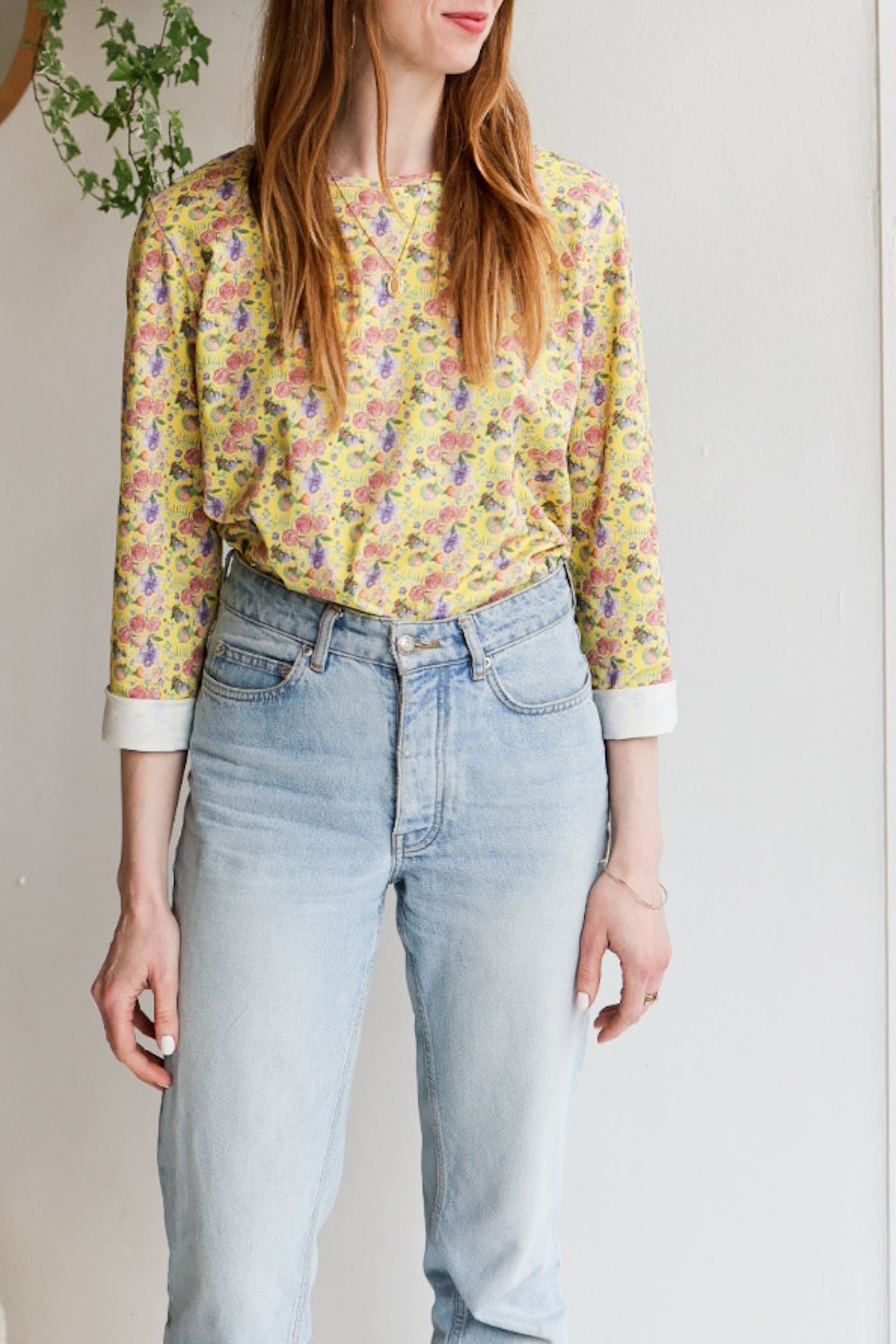 Woman wearing a floral patterned loose long sleeve t-shirt and jeans indoors.