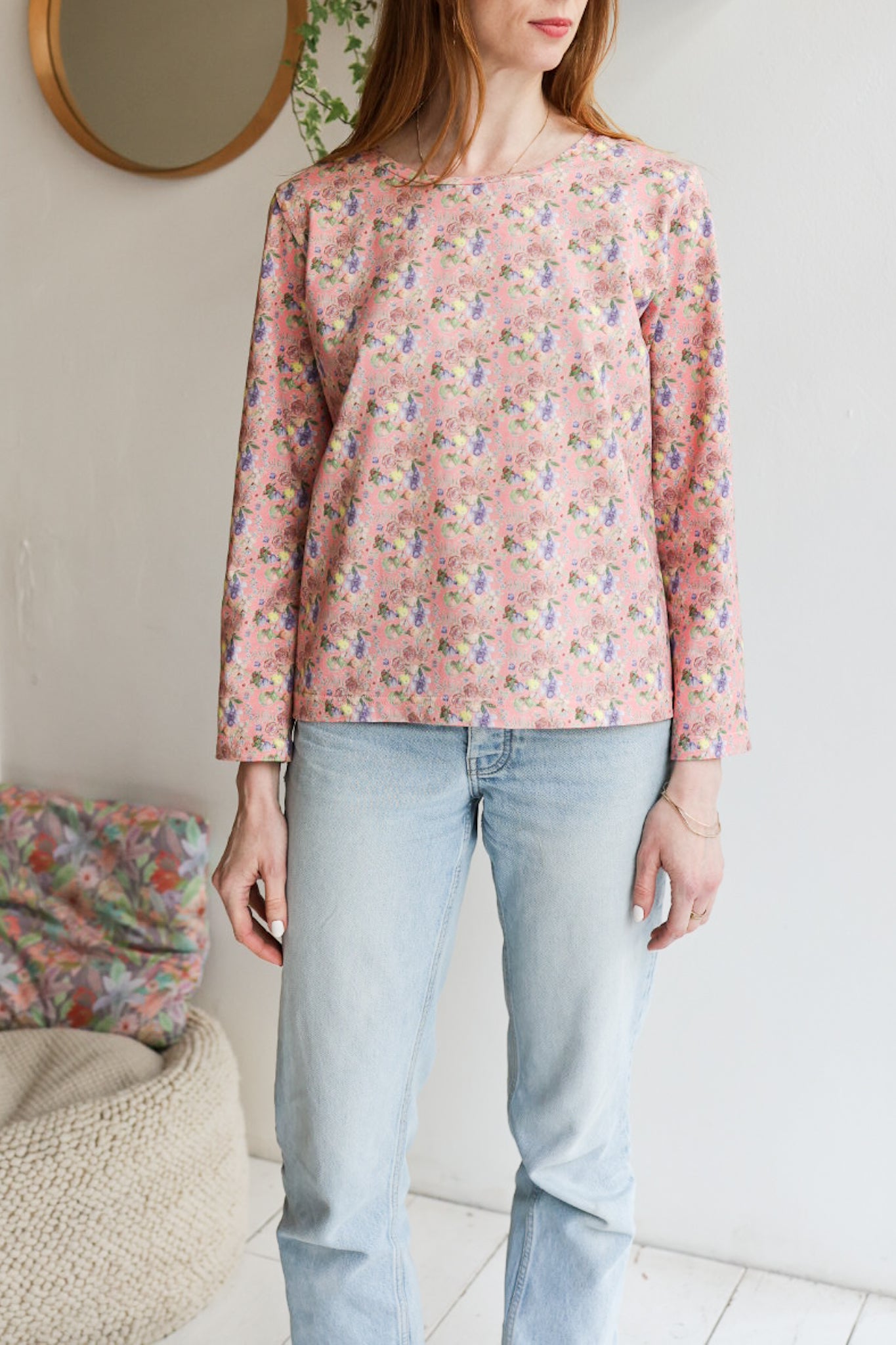 Woman wearing a floral patterned loose long sleeve t-shirt and jeans indoors.