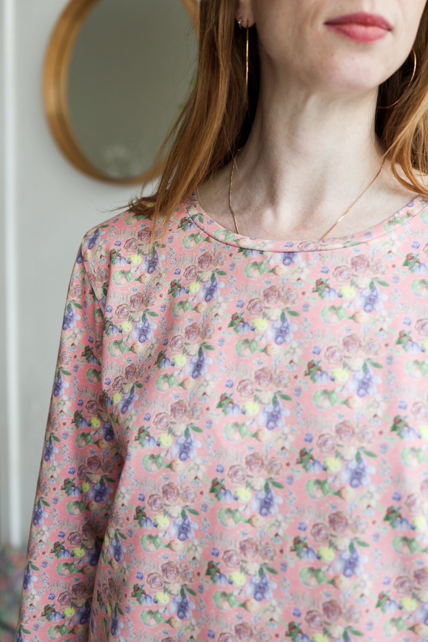 Woman wearing a floral patterned loose long sleeve t-shirt with a blurred background.