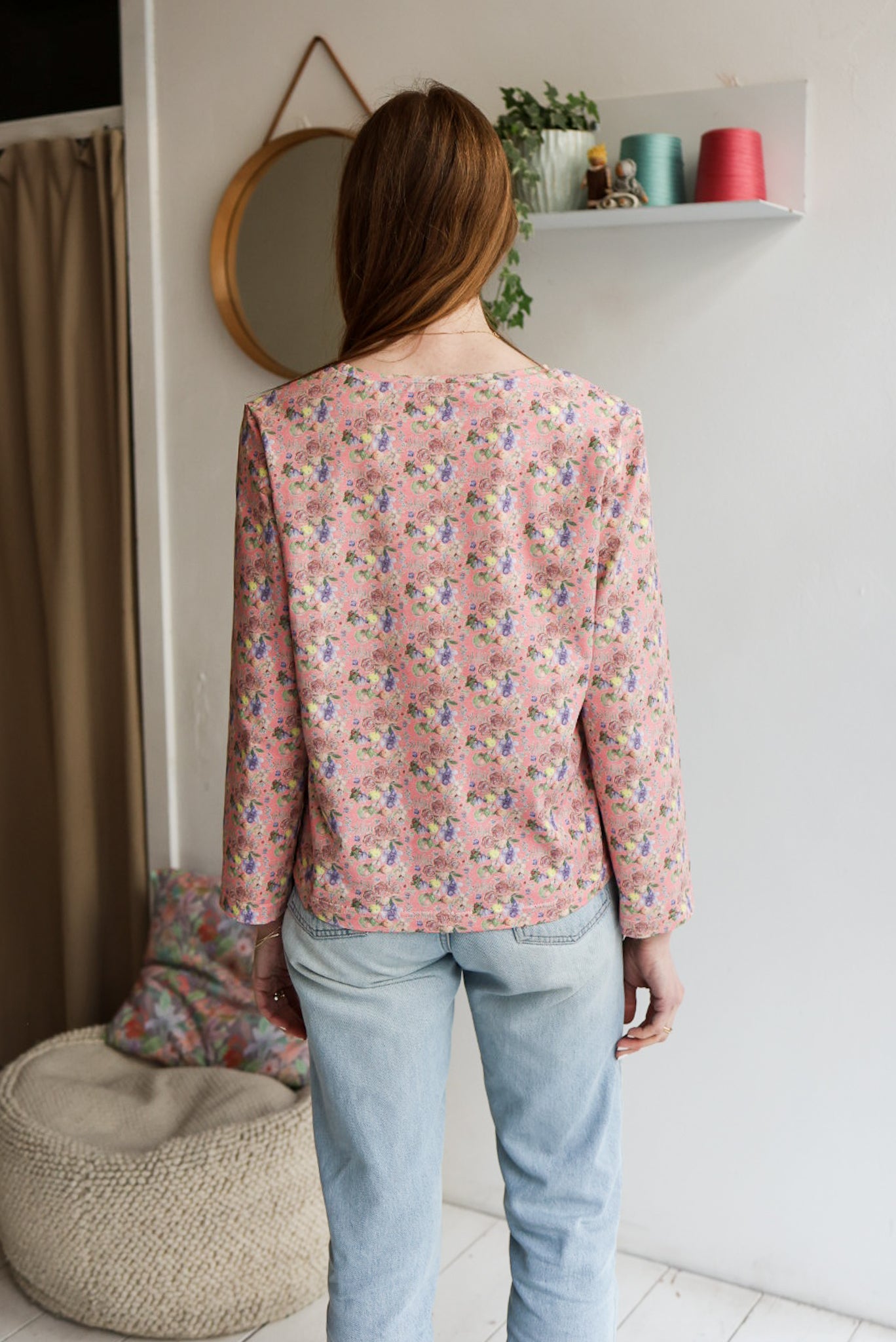 Woman wearing a floral patterned loose long sleeve t-shirt and jeans indoors.