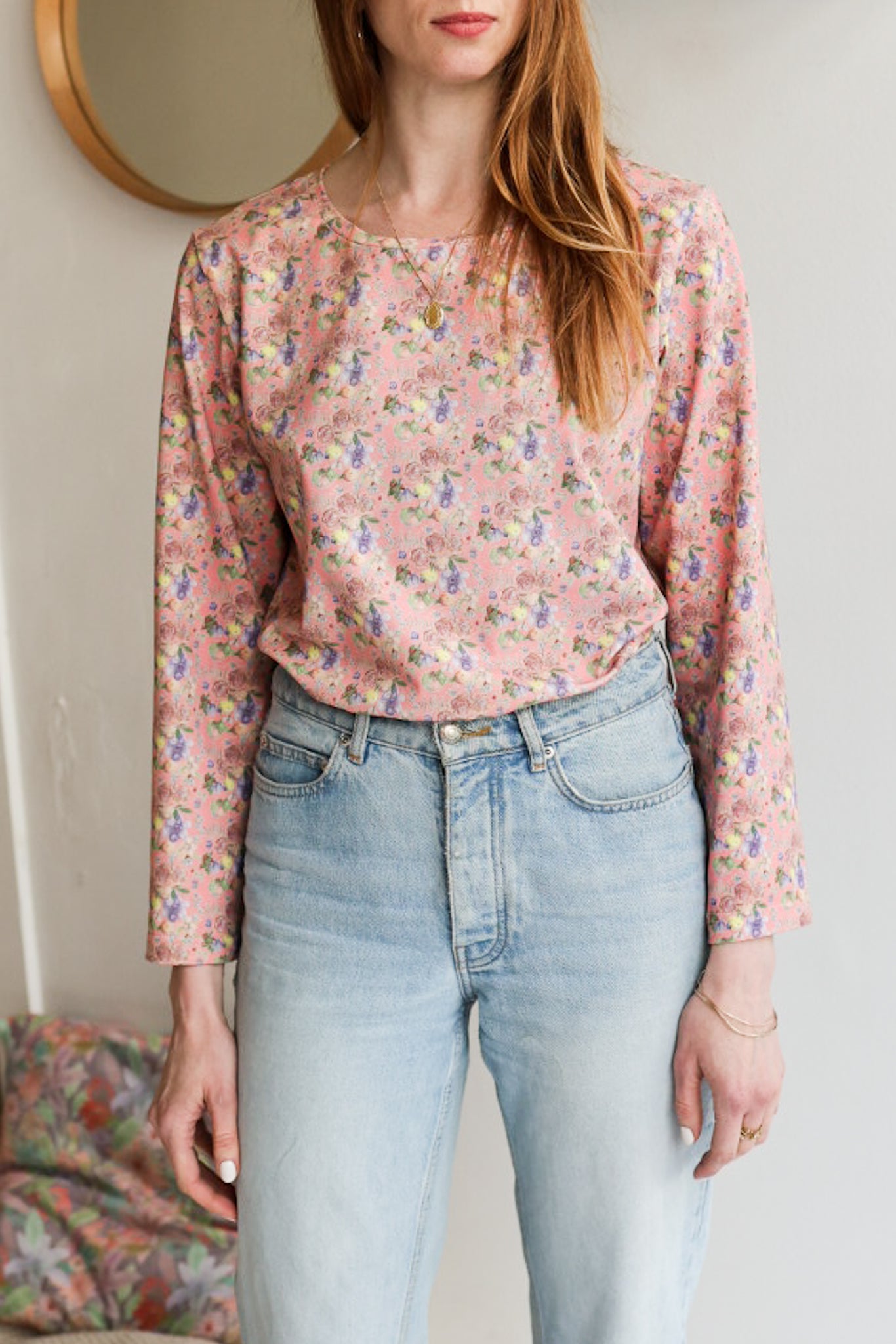Woman wearing a floral patterned loose long sleeve t-shirt and jeans indoors.