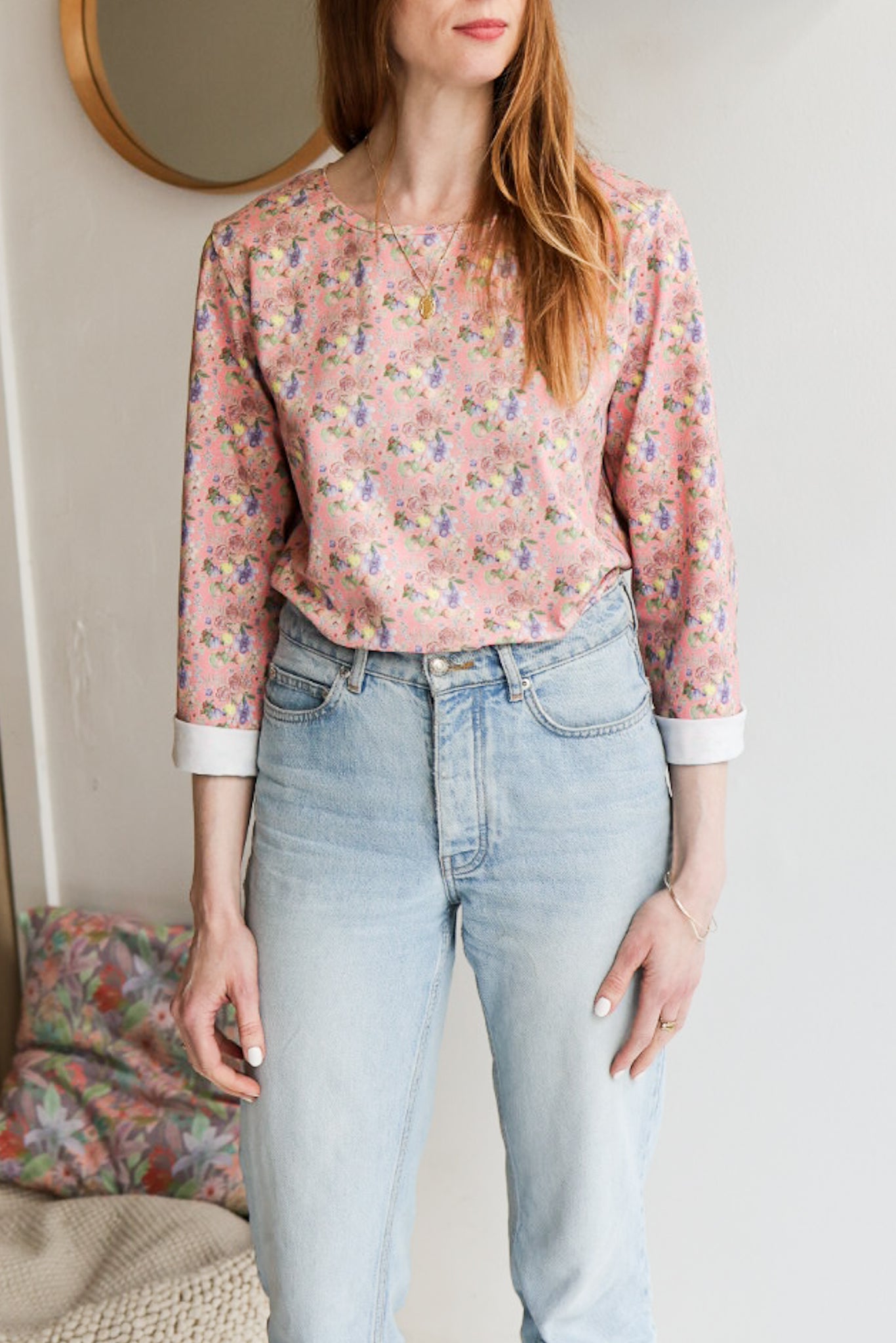 Woman wearing a floral patterned loose long sleeve t-shirt and jeans indoors.