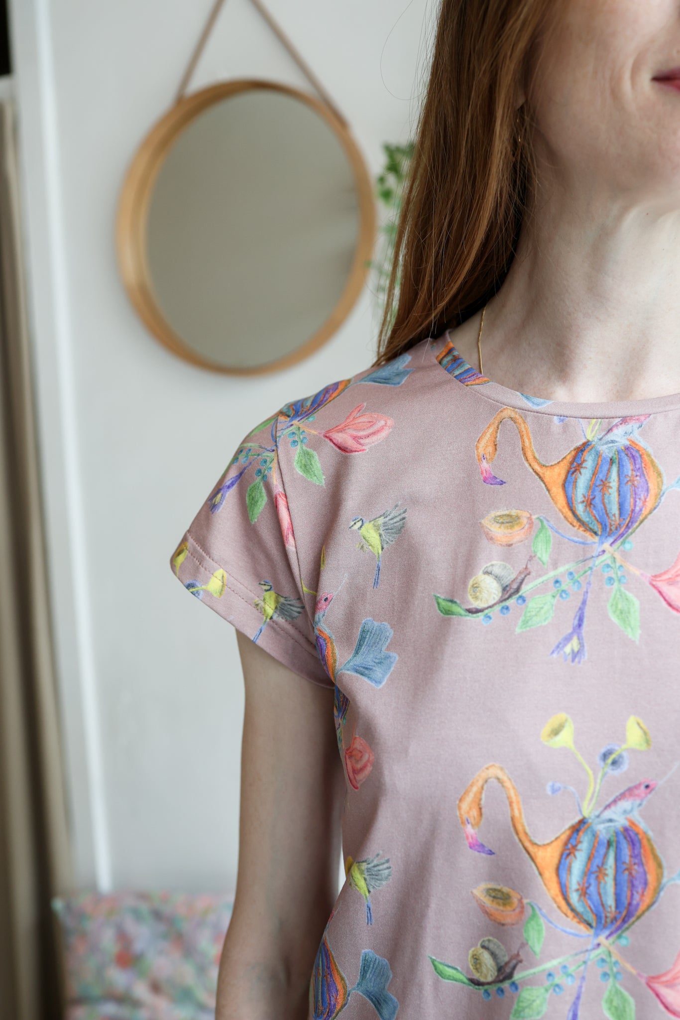 Woman wearing a pink t-shirt with colorful patterns indoors.