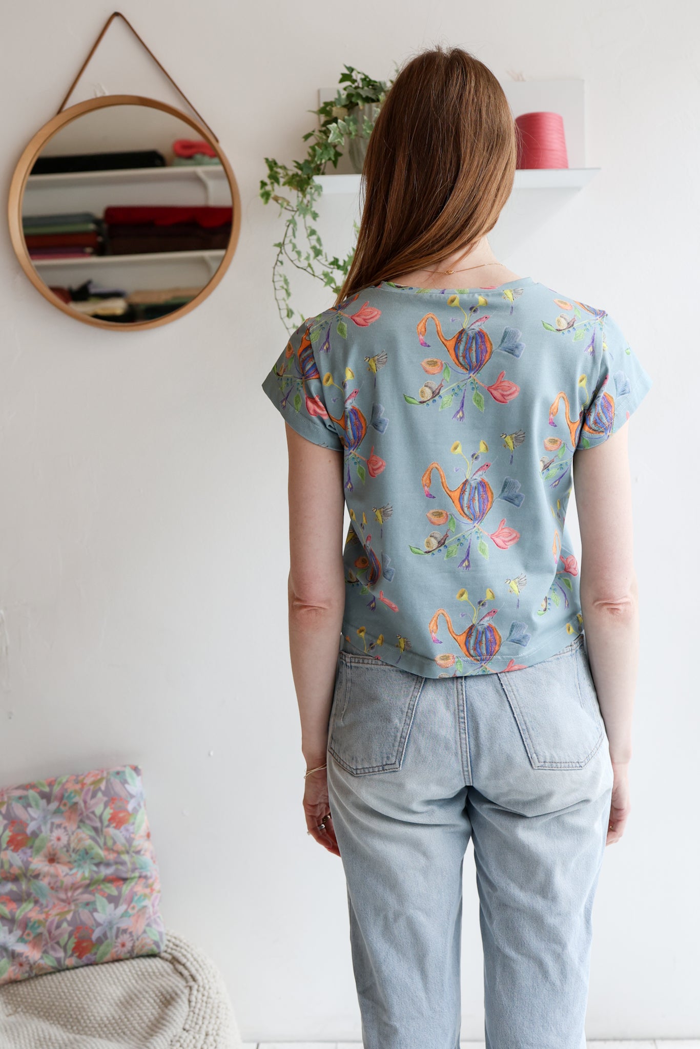 Woman wearing a blue t-shirt with colorful patterns and light blue jeans indoors.
