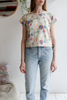 Woman wearing a beige t-shirt with colorful patterns and light blue jeans indoors.