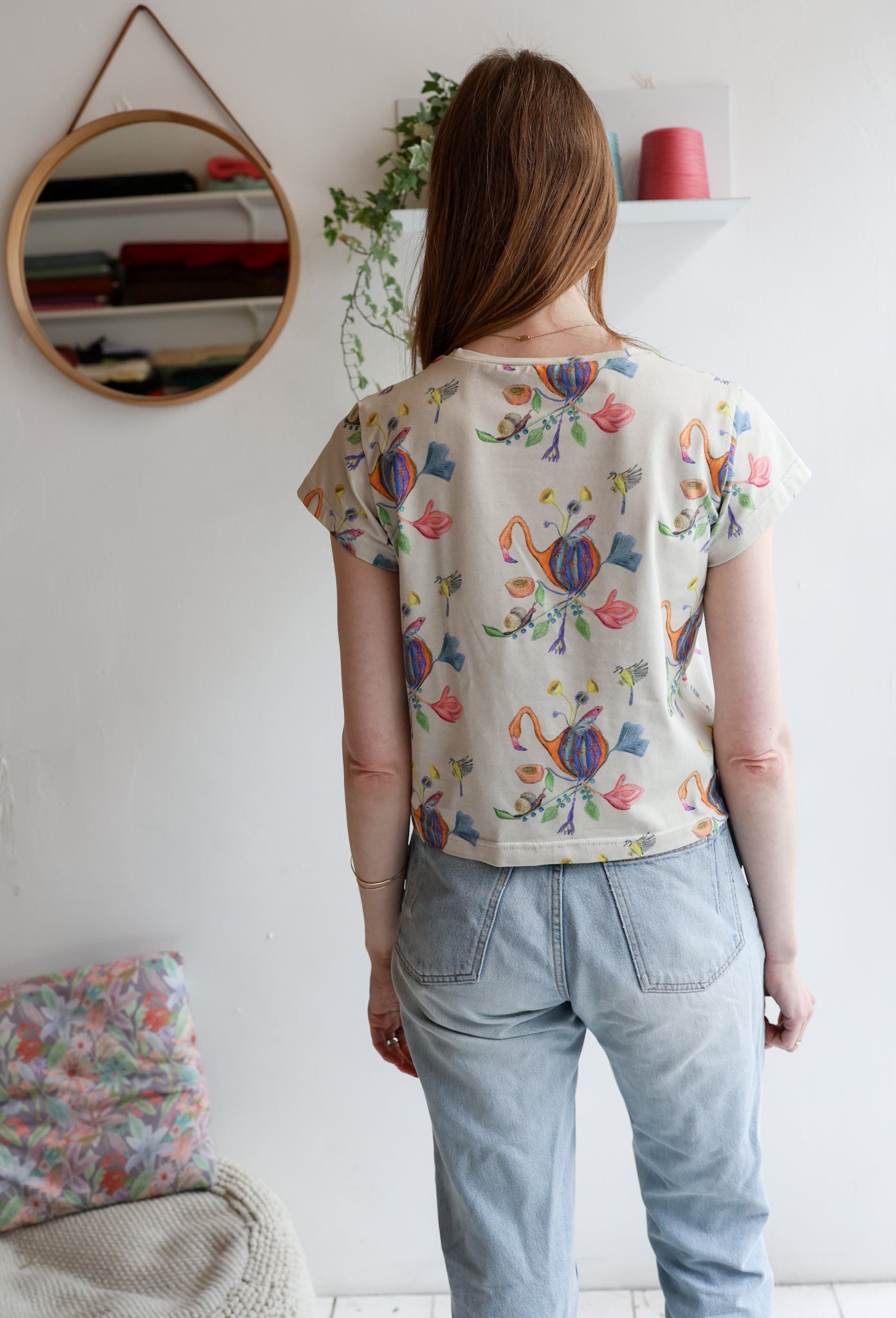 Woman wearing a beige t-shirt with colorful patterns and light blue jeans indoors.